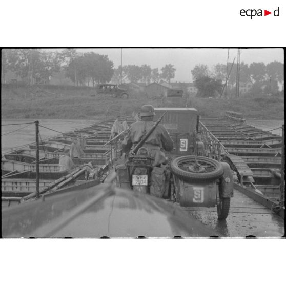 Des éléments d'une batterie d'artillerie 10,5 cm FH 18 traversent un pont flottant assemblé par le Génie allemand.