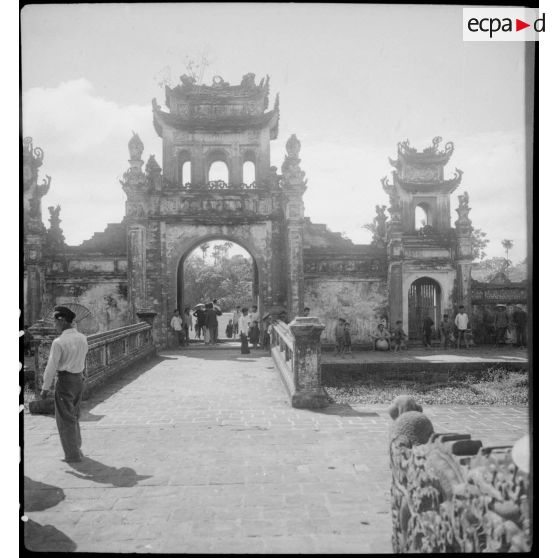 Des vietnamiens flânent devant la porte ornée près de la maison communale à Ha Hoï.