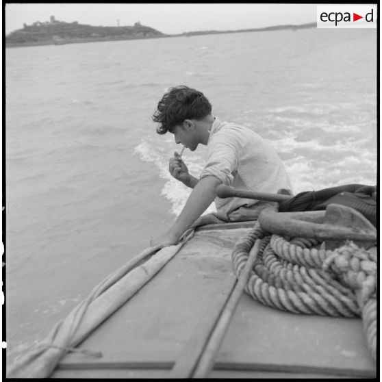 Un marin se brosse les dents à l'arrière d'un chaland de débarquement sur le fleuve Rouge au Tonkin.