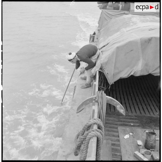 A bord d'un chaland de débarquement, un marin sonde le fond du fleuve Rouge avec une gaffe.