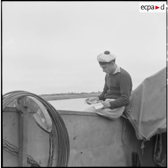 Un marin lisant une lettre à bord d'un chaland de débarquement sur le fleuve Rouge au Tonkin.