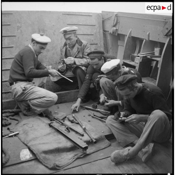 Nettoyage des pièces d'un fusil-mitrailleur à bord d'un chaland de débarquement sur le fleuve Rouge au Tonkin.