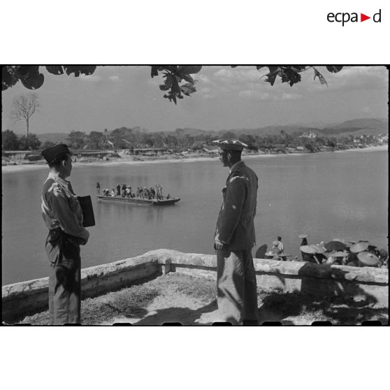 Le commandant Vong A Sang observe le passage d'un bac sur la rivière à Moncay (Mong Cai) en compagnie d'un militaire.