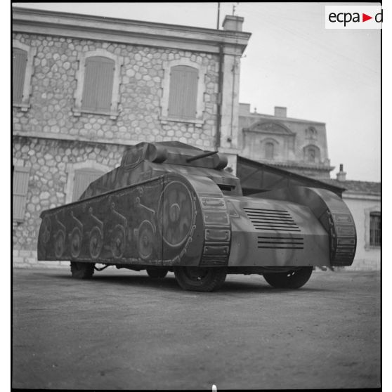 Présentation de trois quarts en contre-plongée d'une maquette de char montée sur une Peugeot 402 dans le parc d'artillerie de Marseille.