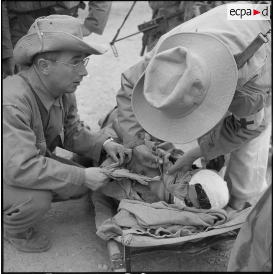 Un tirailleur blessé par un soldat du Viêt-minh embusqué dans les environs d'Ap Van Long est ramené sur une civière et reçoit les premiers soins.