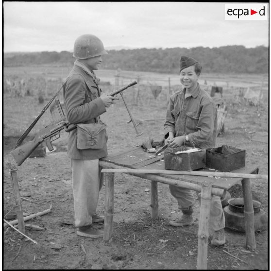 De retour de patrouille au col des Ananas, un fantassin vietnamien, muni d'un fusil-mitrailleur (FM) 24-29, discute avec un cuisinier.