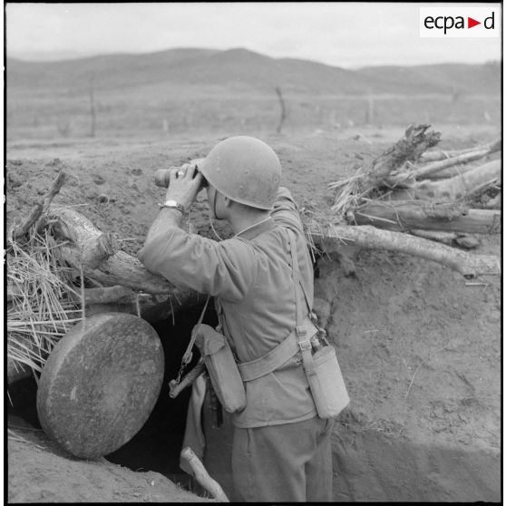 Un sergent de la 9e compagnie du 3e bataillon du 21e régiment d'infanterie coloniale (3/21e RIC) observe aux jumelles depuis une tranchée du point d'appui du col des Ananas.