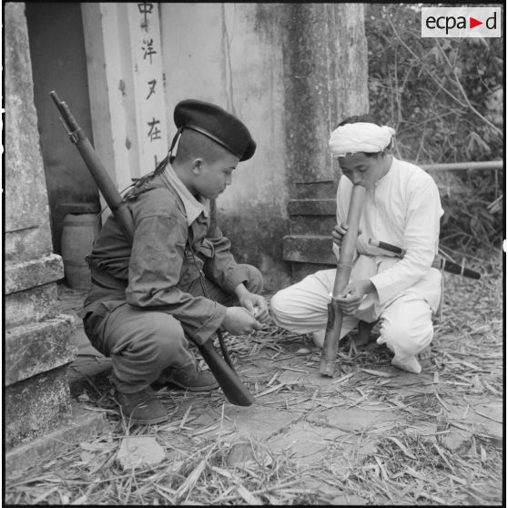 Un tirailleur muong observe un fumeur de pipe à eau.