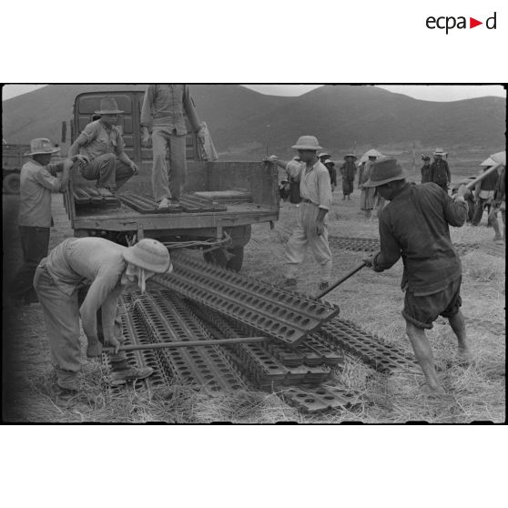 Des travailleurs tonkinois posent des plaques d'acier perforées (PSP) pour l'aménagement du terrain d'aviation de Kien An.