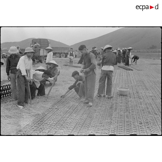 Des travailleurs tonkinois posent des plaques d'acier perforées (PSP) pour l'aménagement de la piste du terrain d'aviation de Kien An.