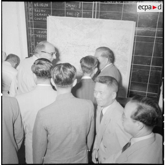 Exposé du général d'armée Jean de Lattre de Tassigny devant une carte à des civils viêtnamiens, vus de dos.