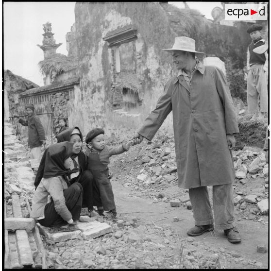 Soldat tenant la main d'un enfant aux côtés de deux villageoises accroupies.