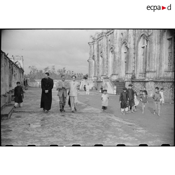 Un prêtre, deux civils et un groupe d'enfants près d'une église.
