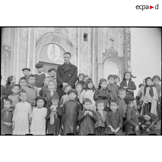 Un prêtre entouré de jeunes enfants vietnamiens devant une église.