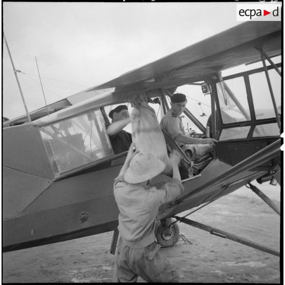 Chargement des sacs de courriers dans un avion Morane-Saulnier avant un départ en mission dans le delta du Tonkin.