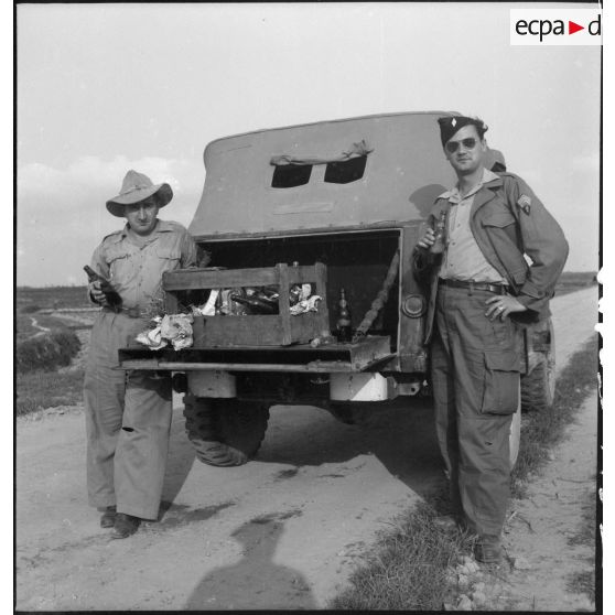 Moment de détente pour deux soldats qui boivent une bouteille à l'arrière d'un véhicule léger stoppé sur une route du Tonkin.