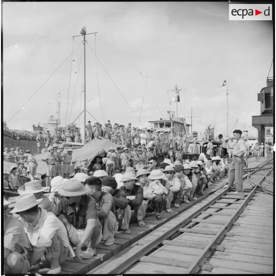 Vietnamiens attendant accroupis sur un quai du port d'Hanoi (Haiphong ?).