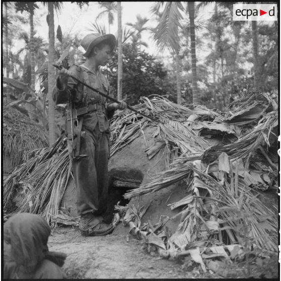 Fouille par un soldat d'une cabane de branchages.