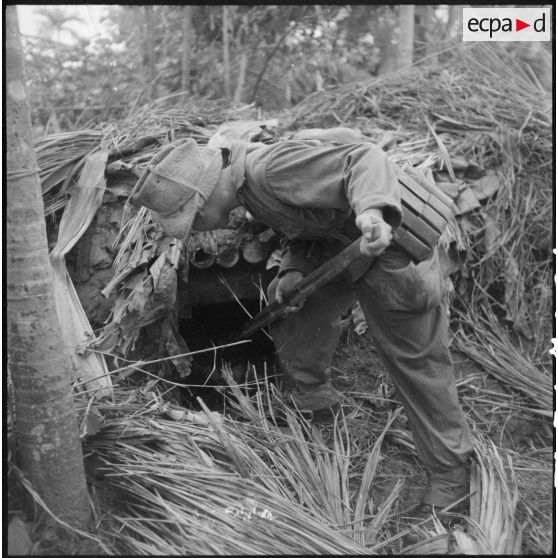 Fouille par un soldat d'une cabane de branchages.