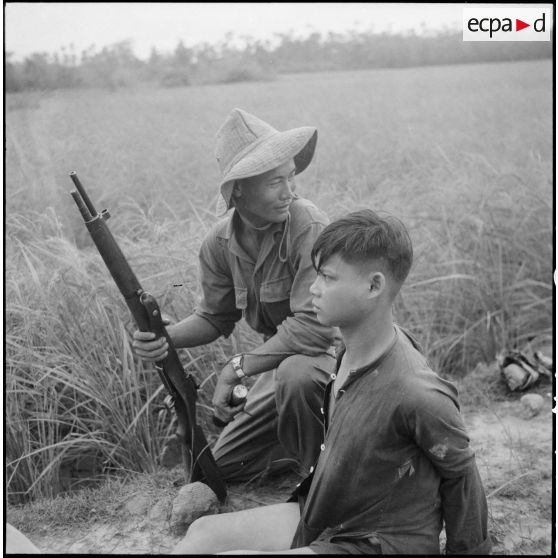 Soldat, l'arme au poing, en compagnie d'un prisonnier ligoté.