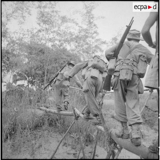 Progression des troupes françaises sur un pont de bambou.