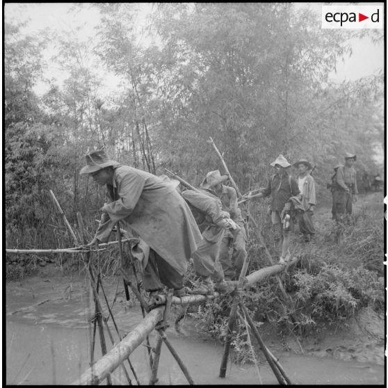 Progression des troupes françaises sur un pont de bambou.