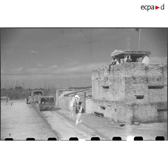 Passage des troupes en camion devant un poste fortifié.