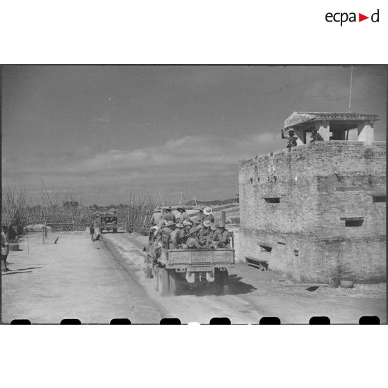 Passage des troupes en camion devant un poste fortifié.
