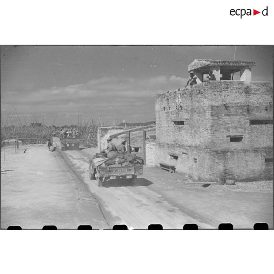 Passage des troupes en camion devant un poste fortifié.