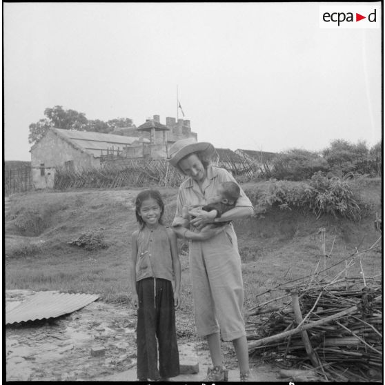 Une assistante sociale tient un bébé dans ses bras. A côté d'elle, une petite fille vietnamienne.
