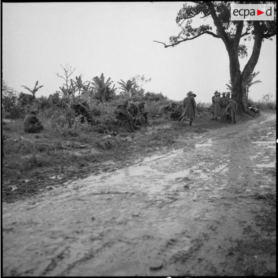 Un groupe de soldats attend sur le bord d'une route détrempée.
