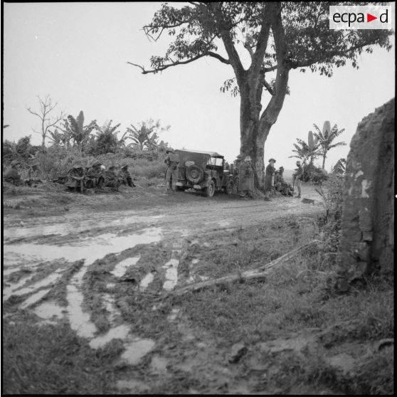Un groupe de soldats attend sur le bord d'une route détrempée.