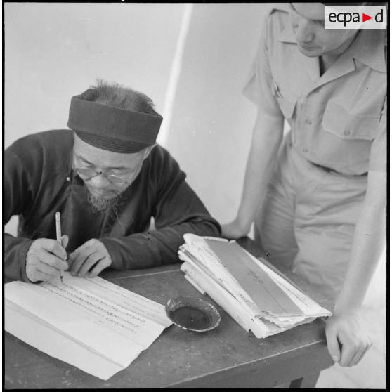 Militaire français du 6e bataillon de parachutistes coloniaux, observant un calligraphe de rue, à Hanoï.