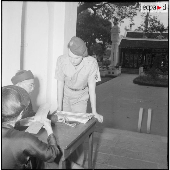 Militaire français du 6e bataillon de parachutistes coloniaux, observant un calligraphe de rue, à Hanoï.