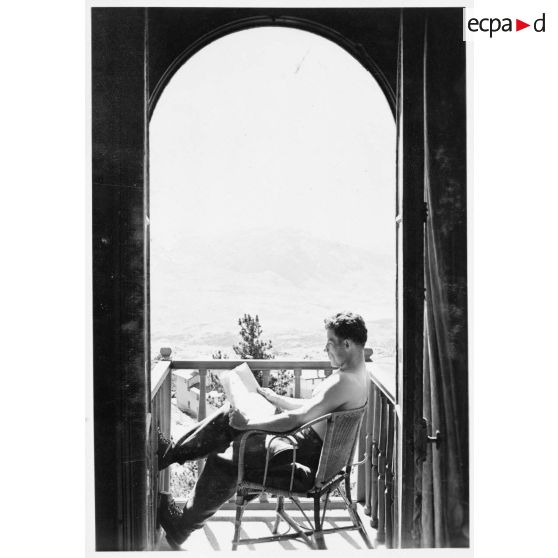Un soldat permissionnaire lit sur le balcon de sa chambre.