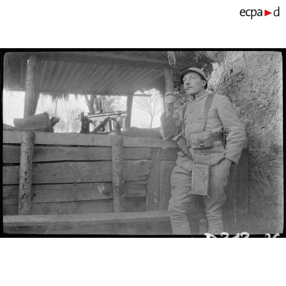 [Un soldat fume la pipe devant une grange].