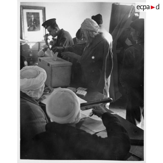Un soldat français et un Algérien dans un bureau de vote en train de voter. [légende d'origine]<br>