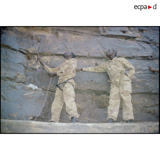 Formation des aides moniteurs commando et des élèves officiers de l'école militaire interarmes d'Atar à l'escalade et au rappel, aux techniques de cordes et d'assurance, au franchissement de fortune, au brancardage dans les falaises de l'Oued Illïj, région d'Atar et d'Azougui. Température d'exercice avoisisant les 40° en raison du rayonnement sur les parois rocheuses, 300 élèves et 10 aides moniteurs ont été formés pendant cette période. [légende d'origine]<br>