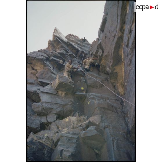 Formation des aides moniteurs commando et des élèves officiers de l'école militaire interarmes d'Atar à l'escalade et au rappel, aux techniques de cordes et d'assurance, au franchissement de fortune, au brancardage dans les falaises de l'Oued Illïj, région d'Atar et d'Azougui. Température d'exercice avoisisant les 40° en raison du rayonnement sur les parois rocheuses, 300 élèves et 10 aides moniteurs ont été formés pendant cette période. [légende d'origine]<br>
