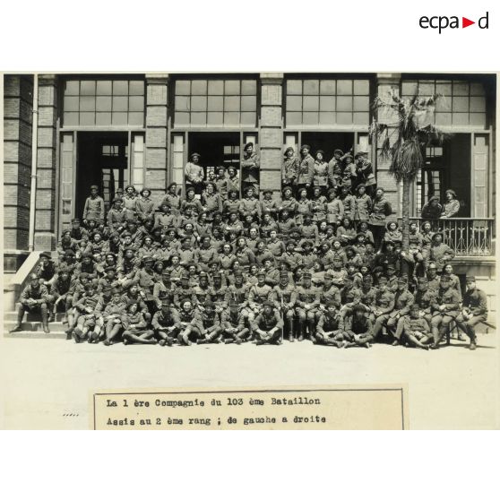La 1re compagnie du 103e bataillon.<br>Assis au 2e rang, de gauche à droite : sergent-clairon DIOT, sergents-chefs FINALTERI et PHILIPPI, adjudant-chef FONTAINE, lieutenant FERROUILLAT, capitaine CARBUCCIA, lieutenant MAZZONI, adjudants BOURLET et VIEULLE, sergent-chef FINIDORI, sergents LECHENE-BIEDERMANN-GIUDICELLI-LE MARREC-CONAS et GALTIERI.<br>Devant le sergent Le Marrec : le sergent VUILLEMIN.<br>Derrière l'adj. VIEULLE : le sergent-chef VALENTI." [légende d'origine]