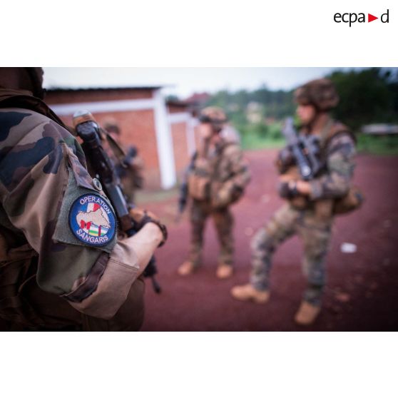 Ecusson de l'opération Sangaris sur la manche de l'uniforme d'un soldat du 3e RG du GTIA (groupement tactique interarmes) Turco écoutant les consignes lors d'un briefing pendant une action quotidienne VNP (vérification de non pollution) du marché central de Bambari.