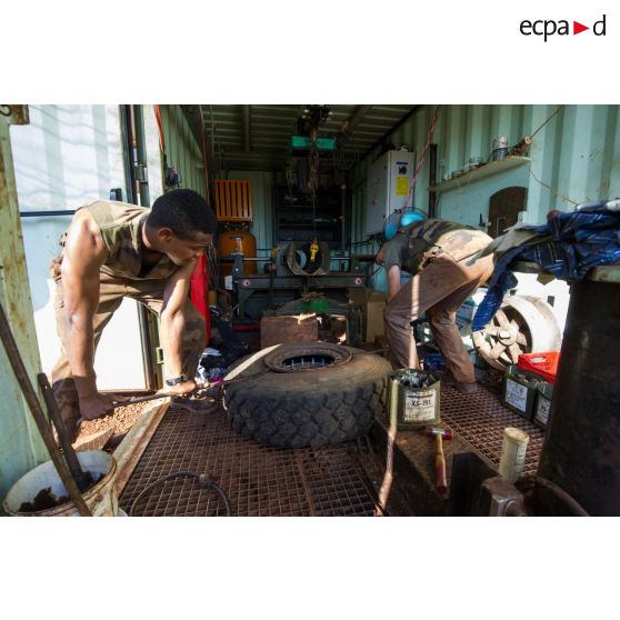Des mécaniciens effectuent une réparation sur la roue d'un véhicule, à l'atelier de réparation mécanique du train de combat du camp de M'Poko de Bangui.