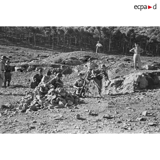 Des jeunes engagés militaires s'entraînent au tir avec un mortier, en montagne, sous le regard d'autorités militaires.