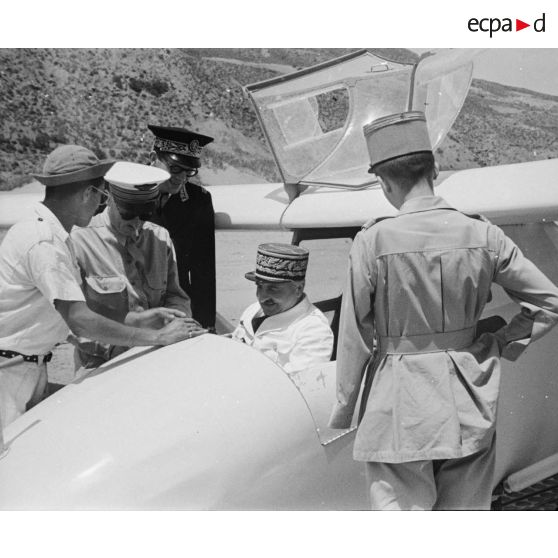 Entouré de personnalités militaires et civiles, le général de corps d'armée Henry Martin, installé dans un planeur, inspecte les commandes et instruments de vol.