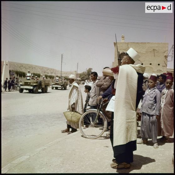 Population civile assistant à un défilé motorisé dans une ville algérienne.