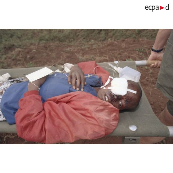 Prise en charge de blessés provenant de Kibeho évacués par hélicoptère par les personnels de l'élément militaire médical d'intervention rapide (EMMIR) à Cyangugu : un enfant blessé à l'oeil et à la tête est brancardé, équipé de sa fiche de tri.
