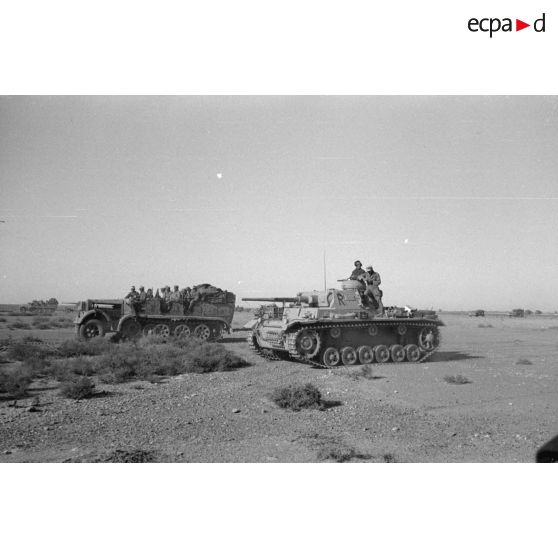 Un tracteur d'artillerie Sd/kfz.7 et une pièce d'artillerie 8,8 cm FlaK devant un blindé Panzer III.