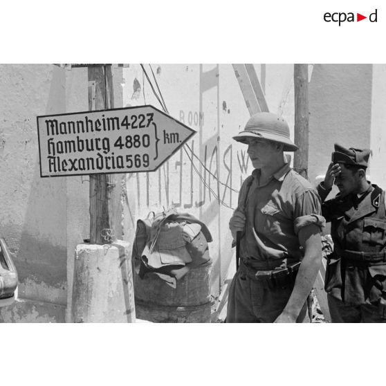 A Bardia, une sentinelle allemande coiffée d'un casque tropical (casque hollandais) et un soldat italien devant un panneau indicateur.