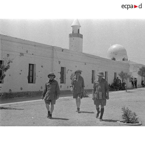 Trois artistes se promènent dans les rues de Bardia. Une mosquée en arrière-plan.