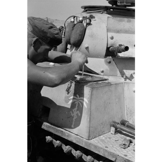 Un homme d'équipage casse des oeufs sur la plaque d'un casier extérieur du Panzer II et les fait cuire.